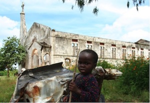 Kind vor Autowrack und zerstörter Kirche in Nigeria