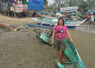 Fischerfrau im zerstörten Boot. Neues Boot des ADRA Netzwerks im Hintergrund